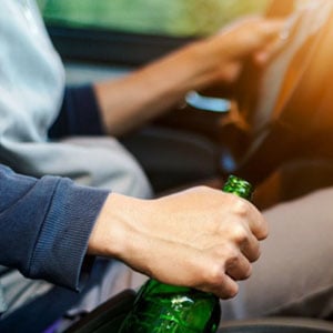 A man holding a beer bottle while driving a car