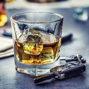 A glass of whiskey with ice next to car keys, symbolizing drinking and driving. 