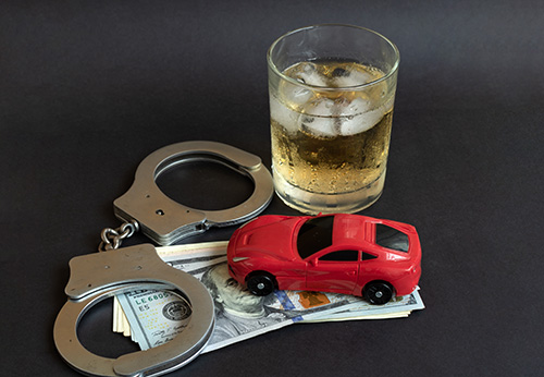 Handcuffs, glass of alcohol, and a toy red car representing a DUI arrest