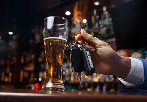 Person holding car keys at a bar next to a tall glass of beer
