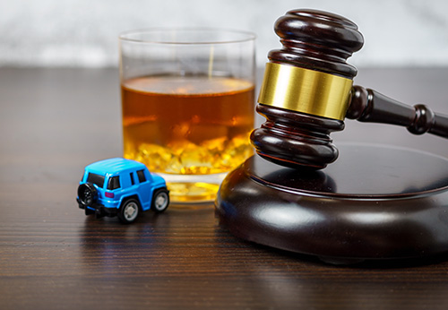 Legal gavel, glass of whiskey, and a small blue toy car on a wooden desk